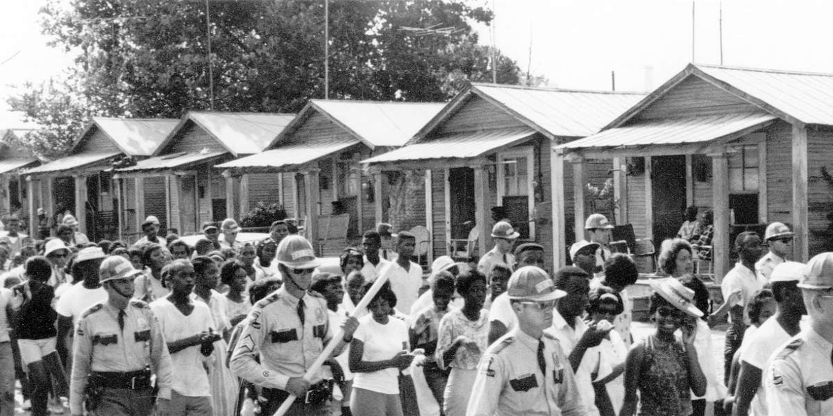 Protesters march past Bogalusa mill houses, flanked by police