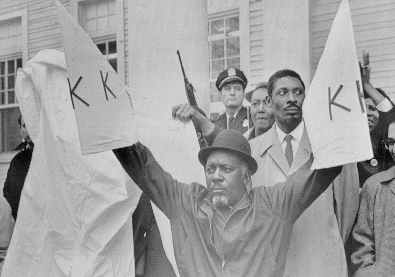 Deacon Charles Sims defiantly holds up 2 mock KKK flags 